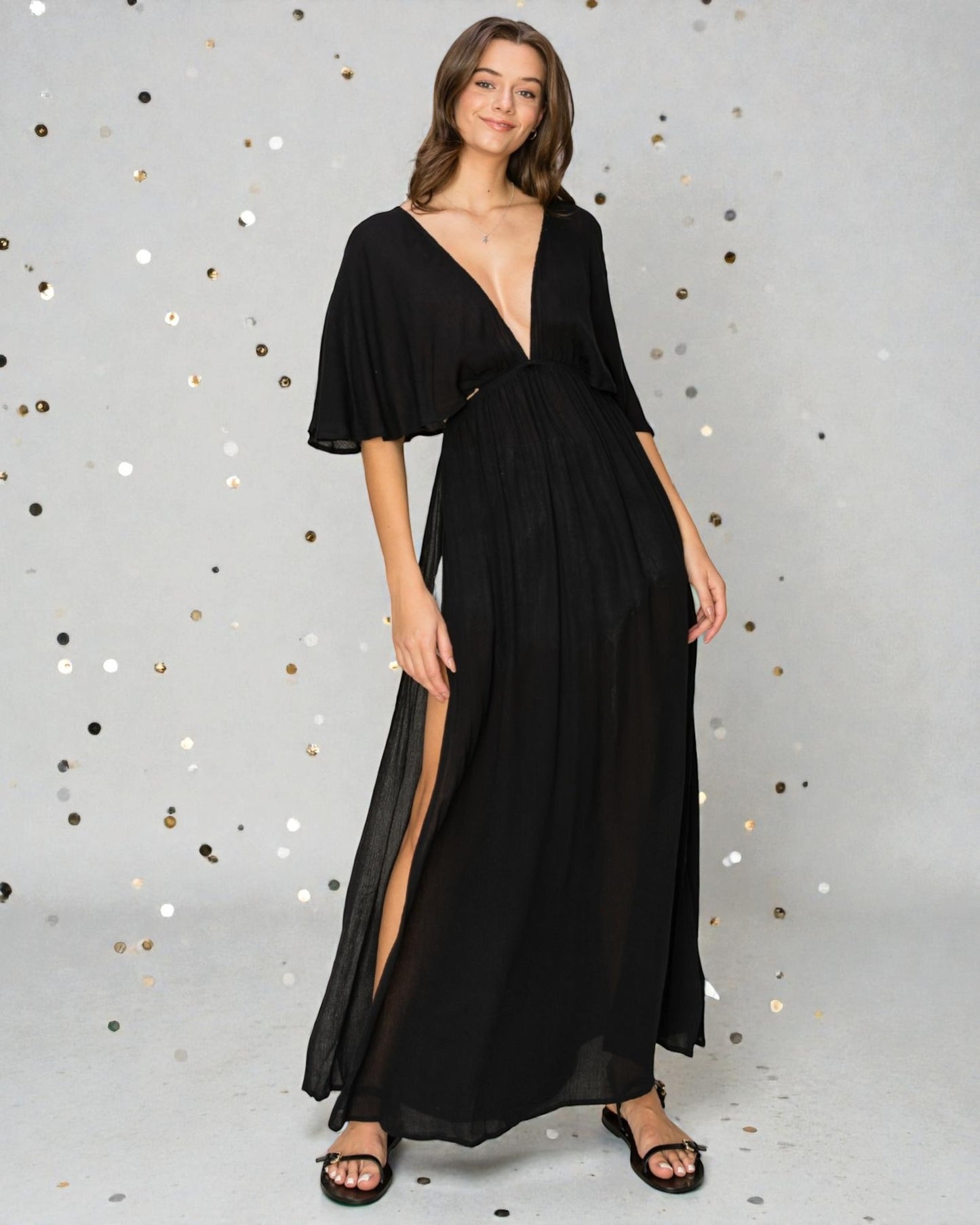 Woman wearing a black evening gown with a deep neckline and slit on a gray background with confetti.