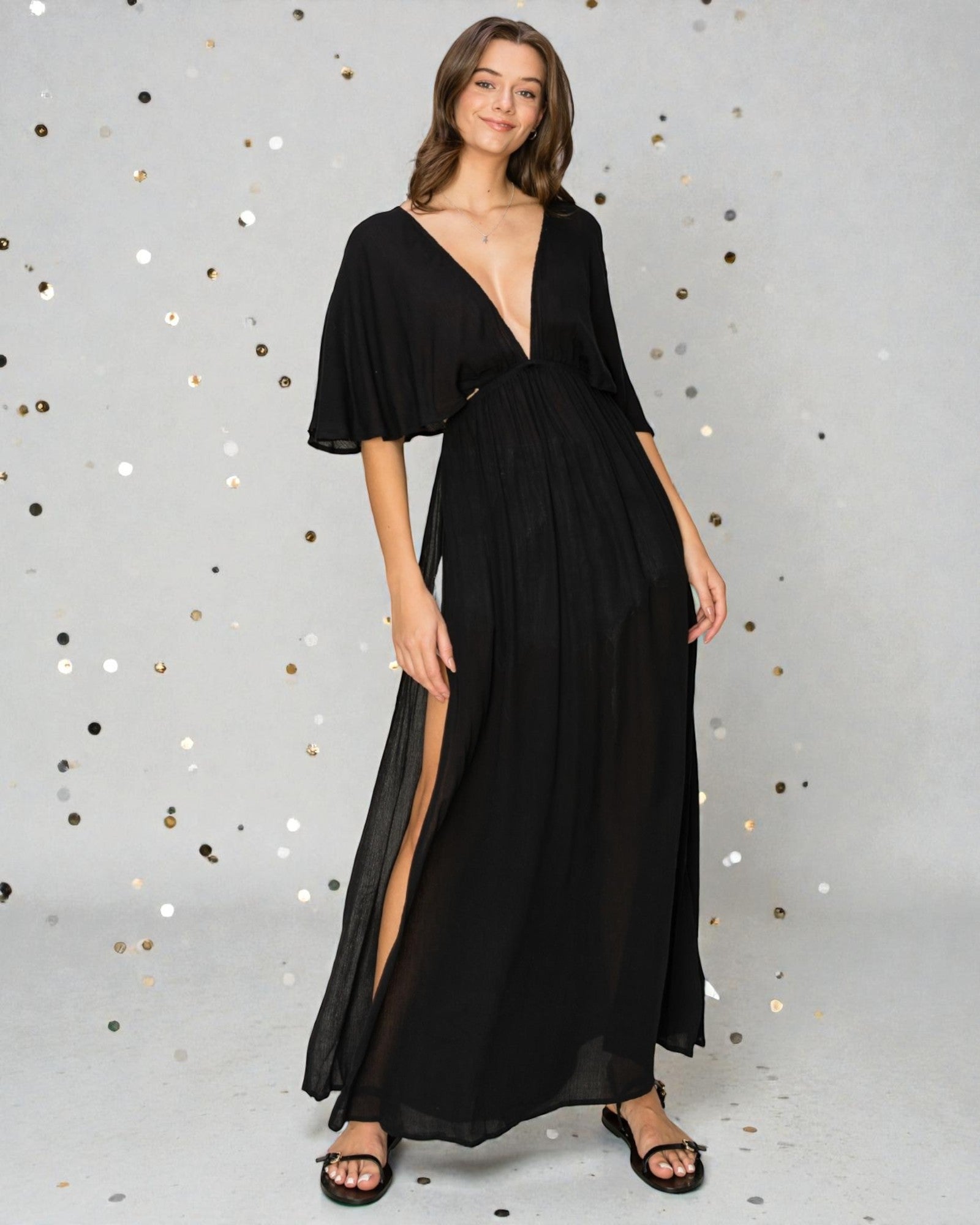 Woman wearing a black evening gown with a deep neckline and slit on a gray background with confetti.