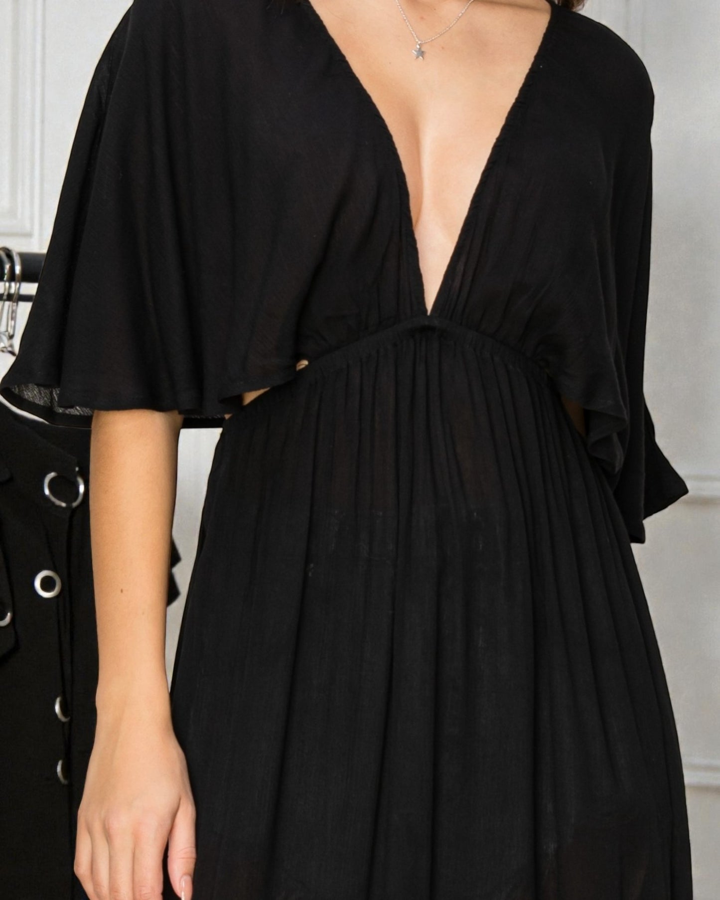 Black dress with a deep neckline and short sleeves on a neutral background