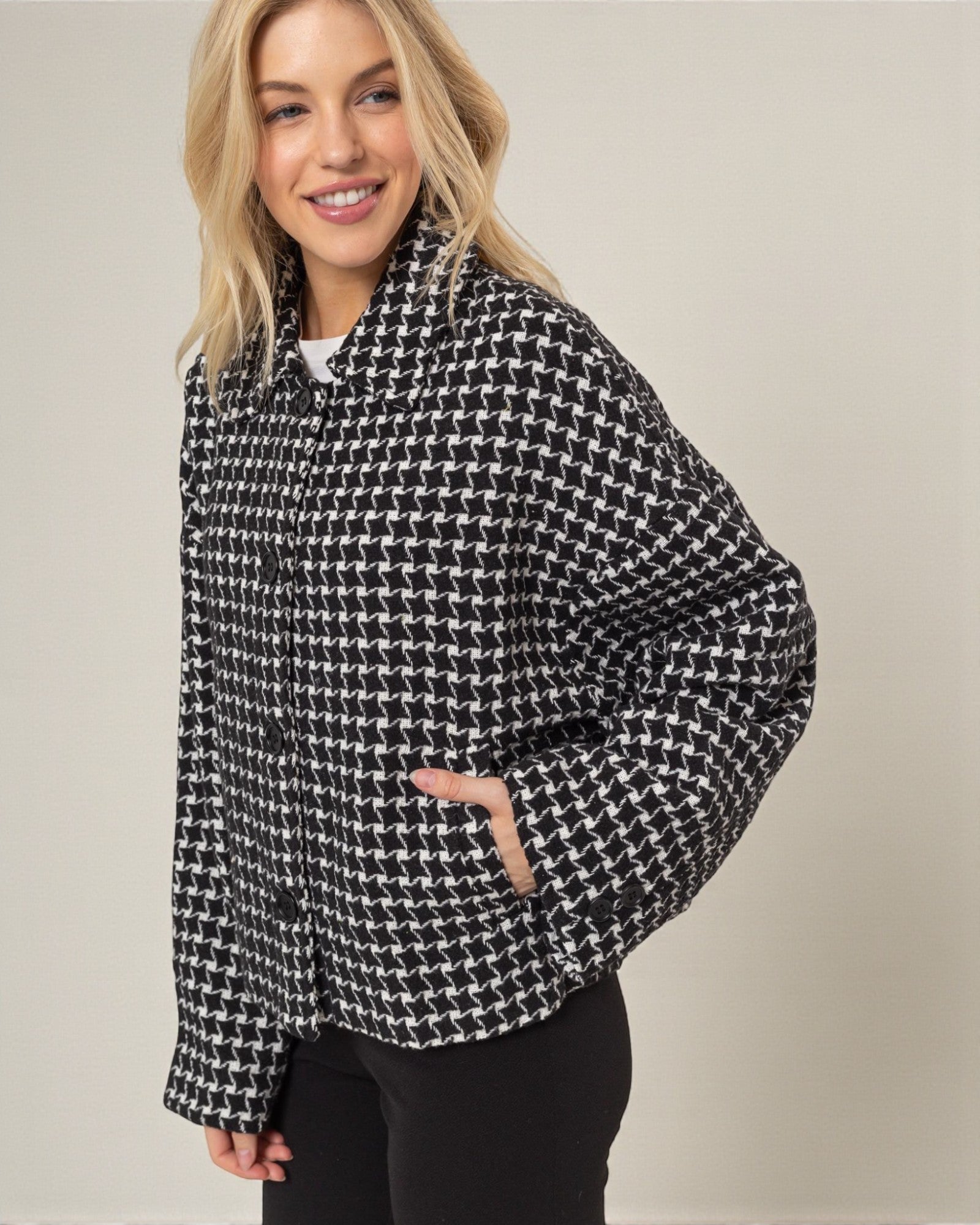 Woman wearing a black and white houndstooth patterned jacket on a plain background