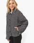 A woman wearing a black and white houndstooth patterned jacket with black pants, photographed against a clean white studio background.