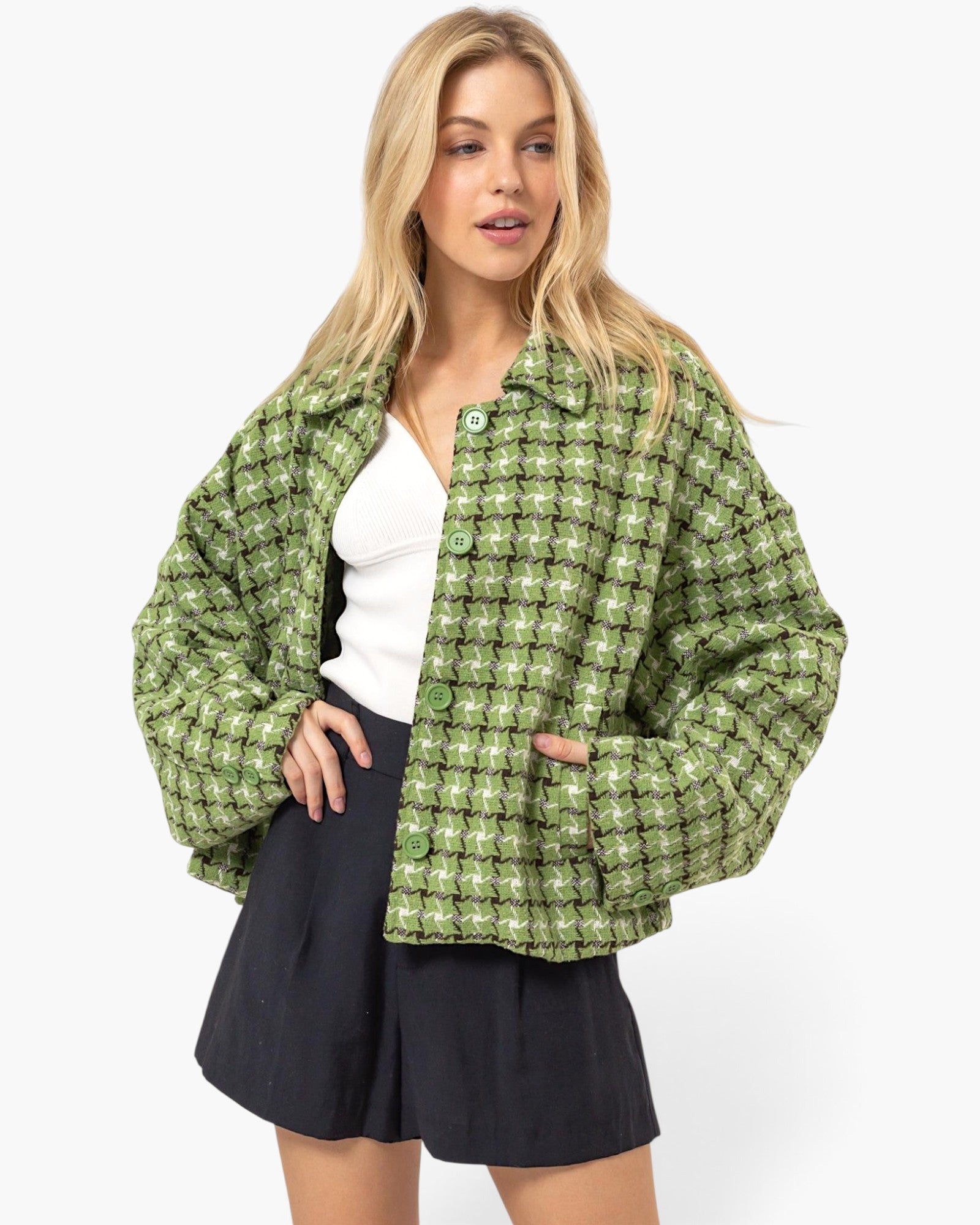 A woman modeling a green and white checkered cropped jacket with a textured bouclé-like fabric, worn over a white top and black skirt against a light gray studio background.