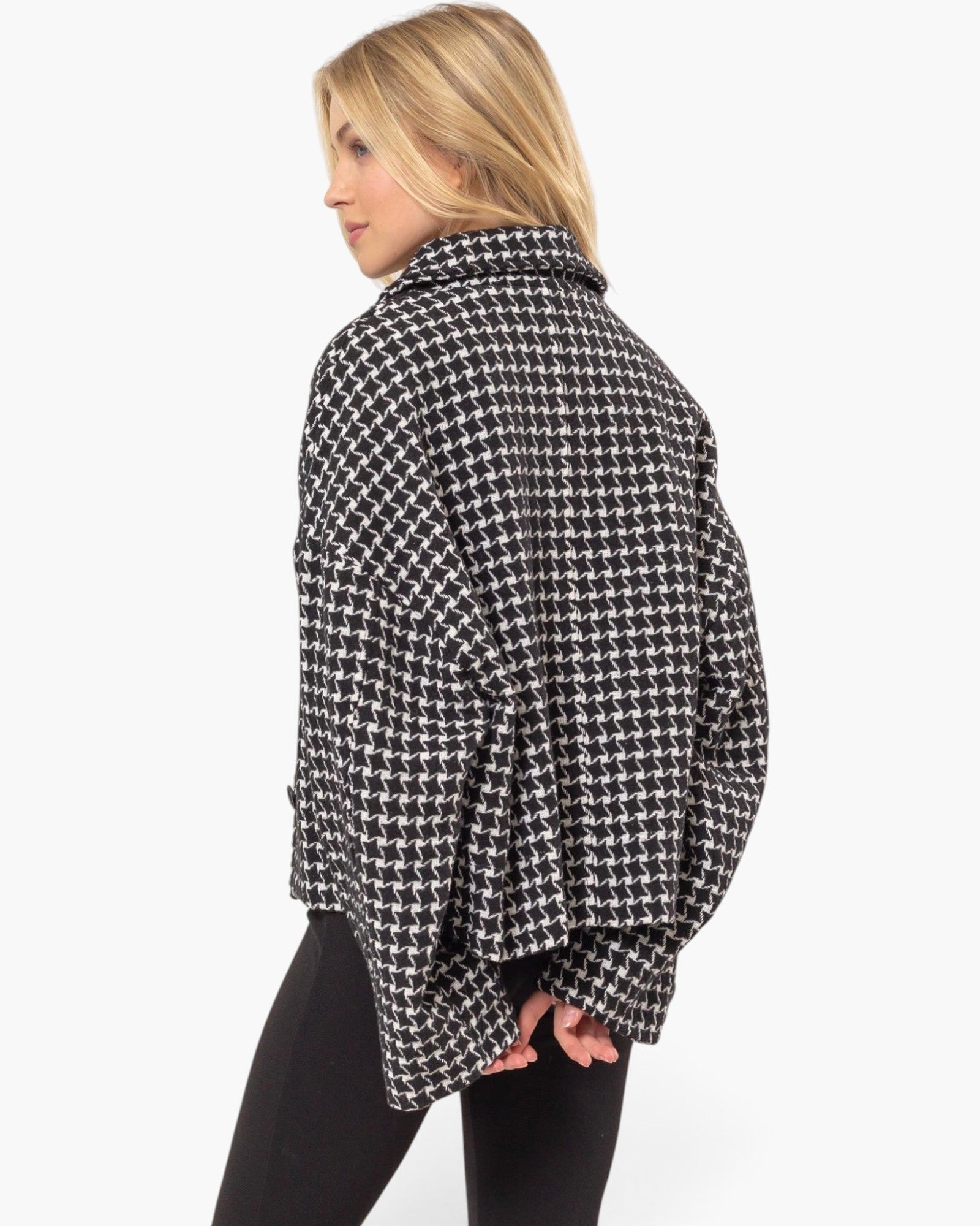 A woman shown from the back wearing a black and white houndstooth patterned oversized jacket or shrug, paired with black leggings, against a plain white studio background.