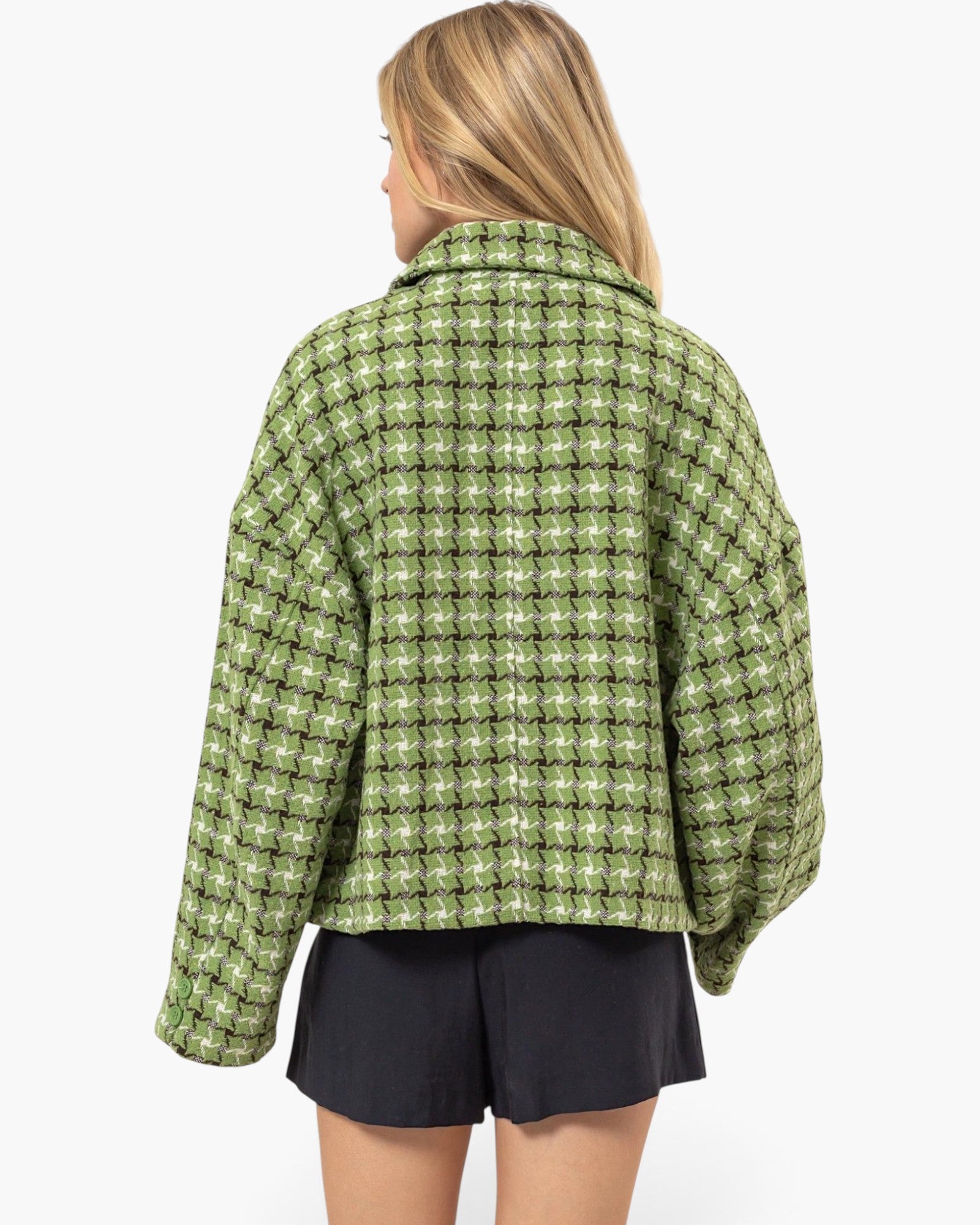 A woman shown from the back wearing an oversized green and white plaid jacket with black shorts, photographed against a plain light gray studio background.
