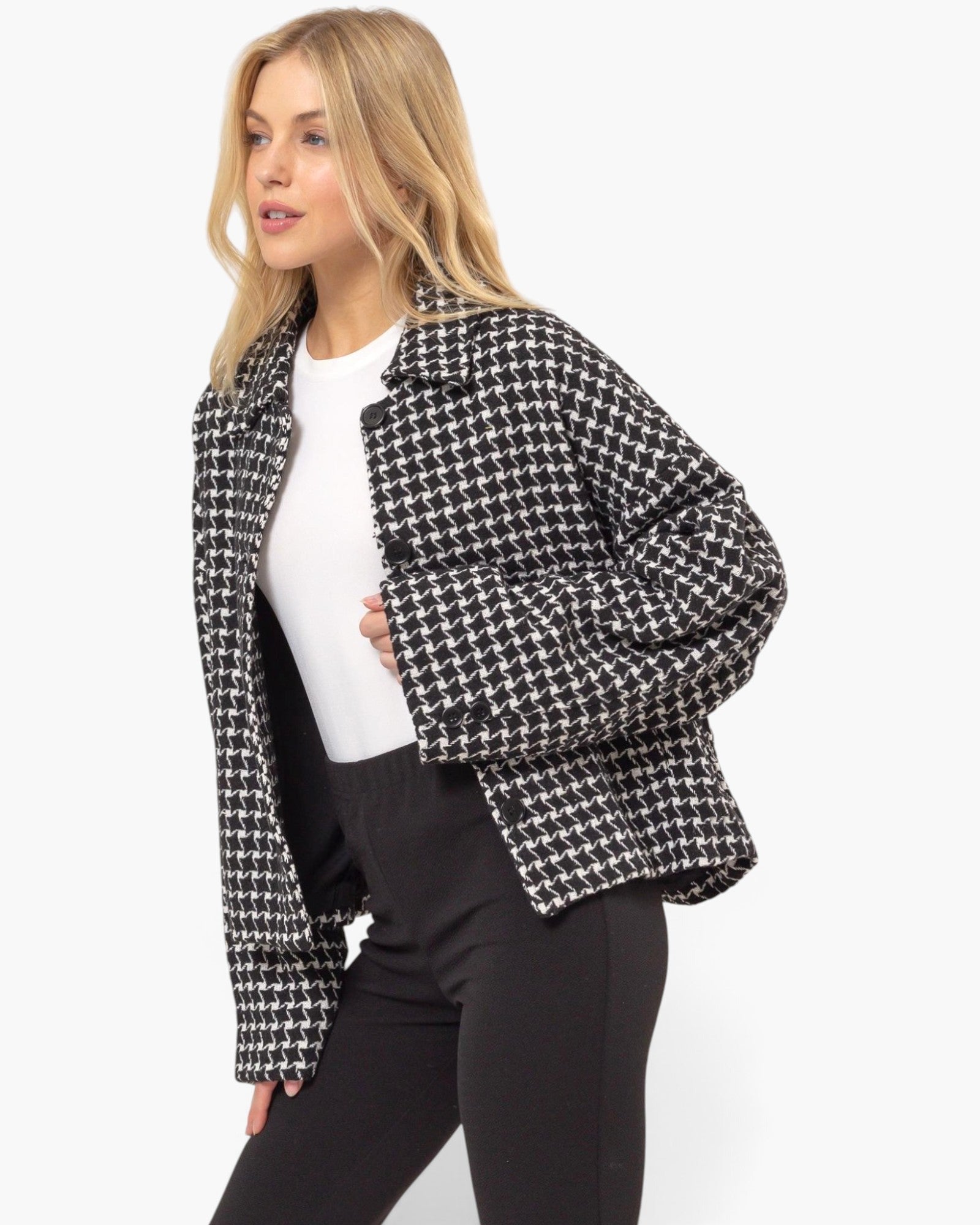 A woman wearing a black and white houndstooth patterned cropped jacket over a white top and black pants, photographed against a clean white studio background.