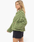 A woman wearing a green and white plaid button-up shirt jacket with black shorts, shown from a side profile against a plain white studio background.