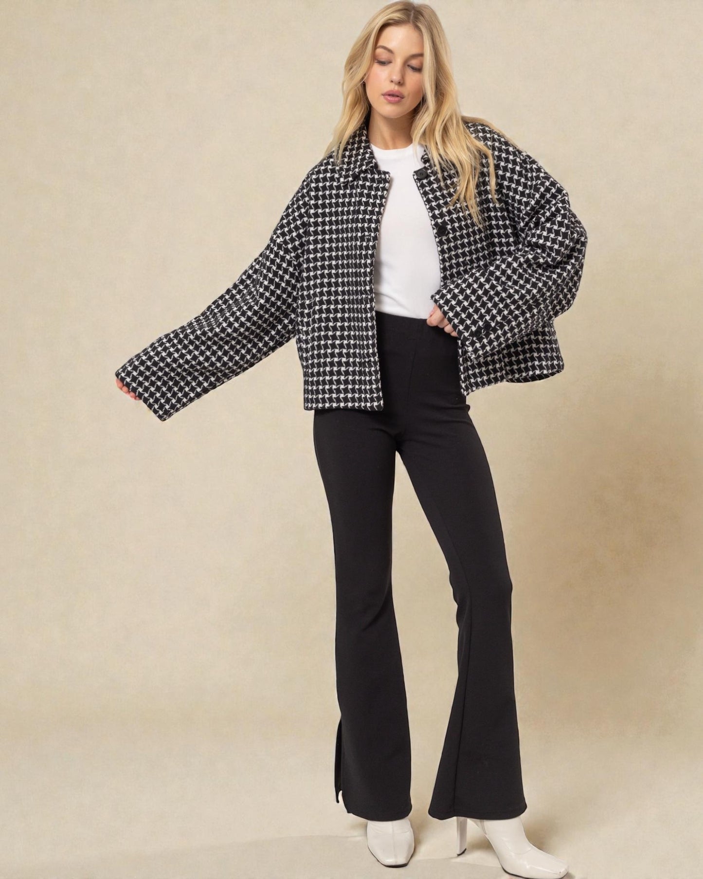 Woman wearing a black and white checkered jacket with black flared pants on a beige background