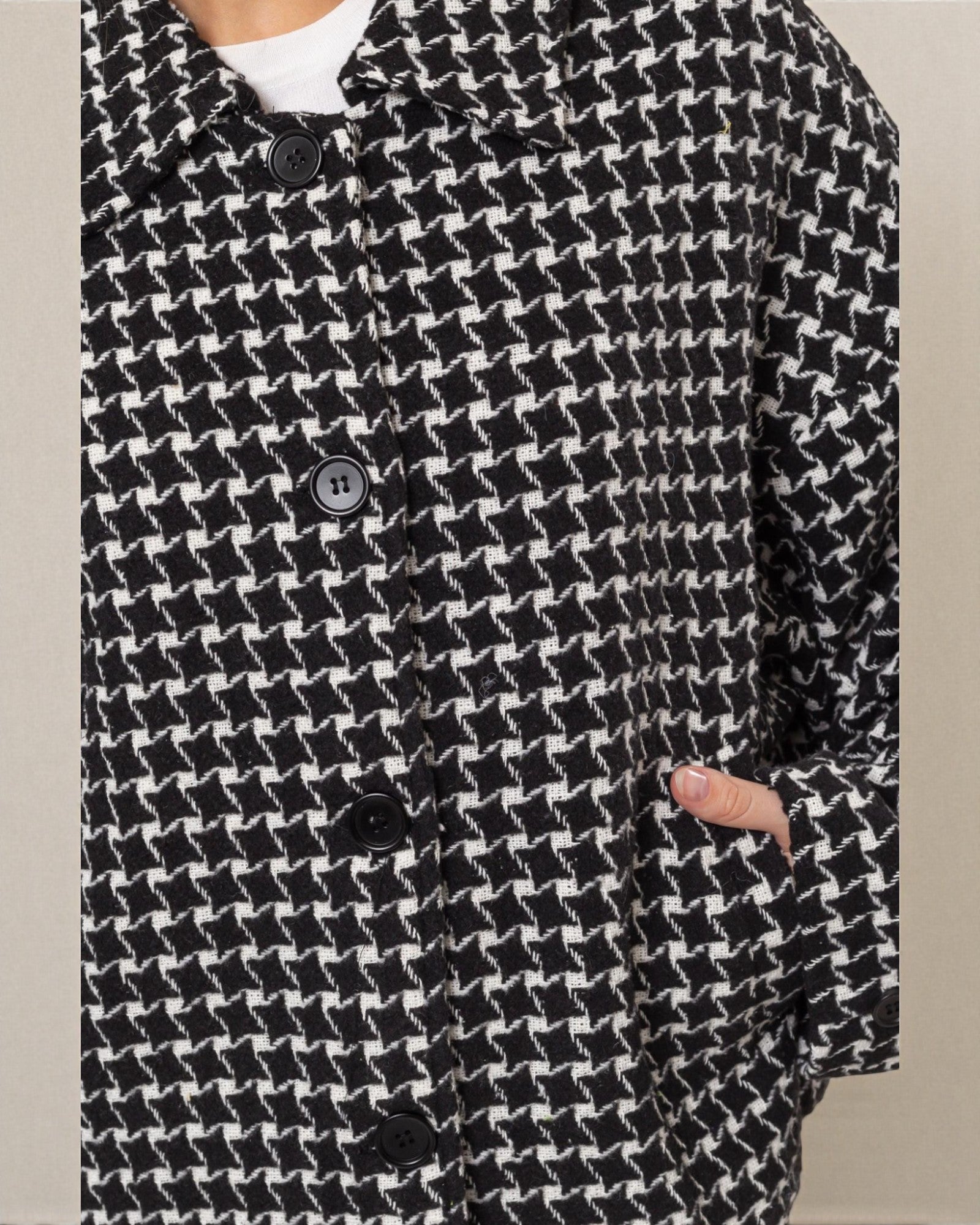 Black and white houndstooth patterned coat with button details on a neutral background