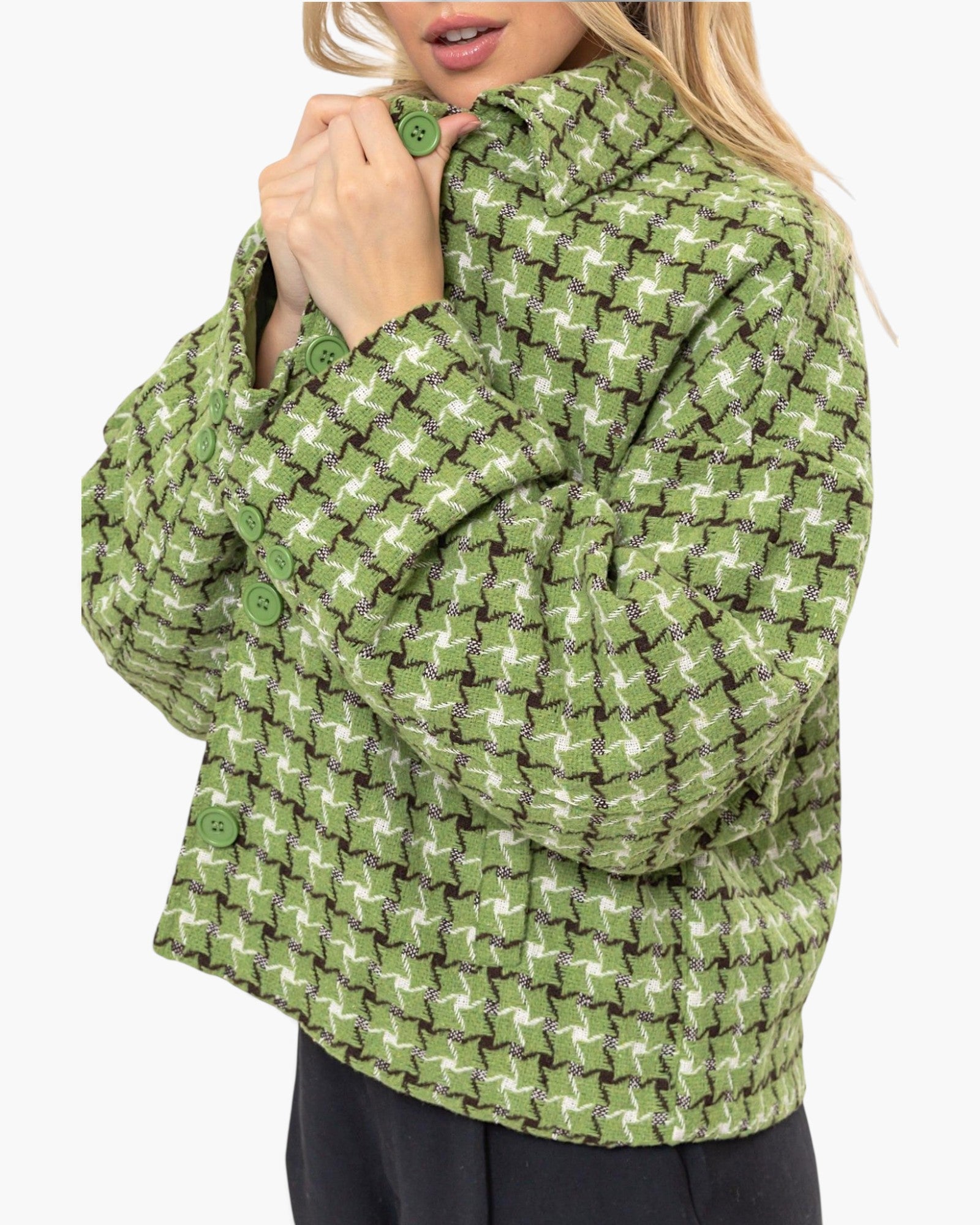 A woman wearing a cropped knit cardigan with a green, white, and brown houndstooth-like pattern, shown against a plain light gray background.