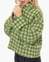 A woman wearing a cropped knit cardigan with a green, white, and brown houndstooth-like pattern, shown against a plain light gray background.