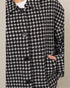 Black and white houndstooth patterned coat with button details on a neutral background