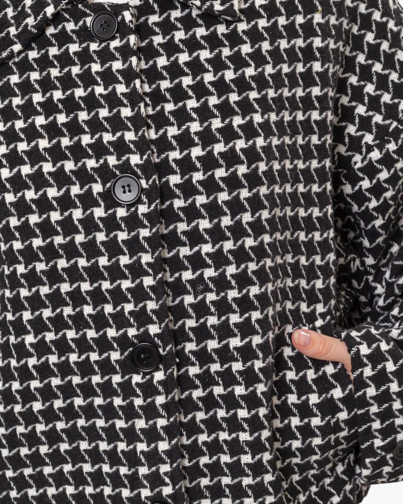 Close-up of a black and white houndstooth patterned jacket with dark buttons and a hand pocket showing a finger.