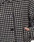 Close-up of a black and white houndstooth patterned jacket with dark buttons and a hand pocket showing a finger.