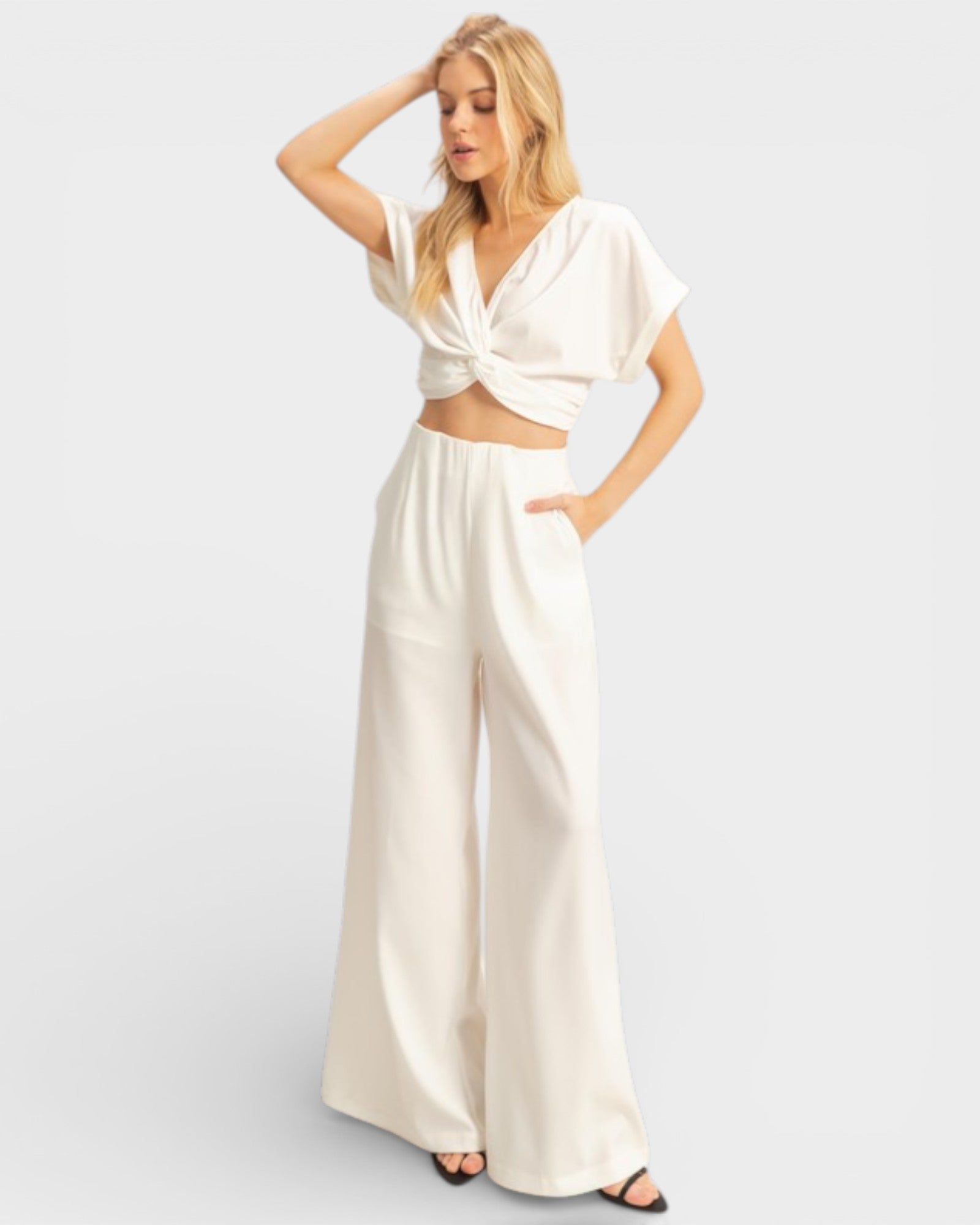Woman wearing a white outfit with wide-leg pants on a light gray background