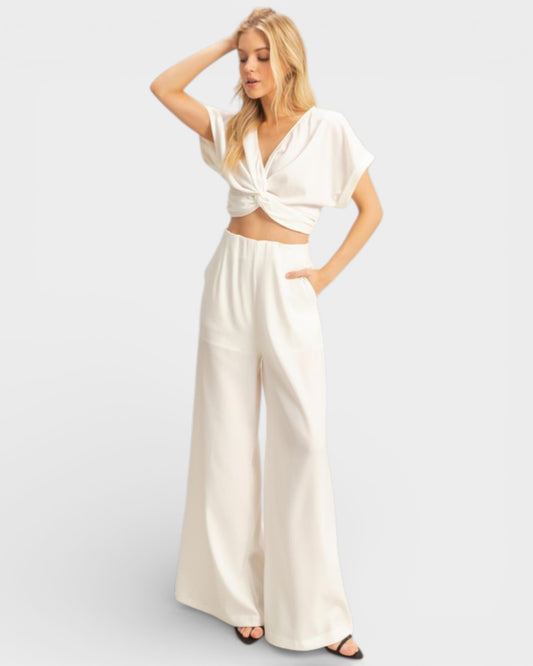 Woman wearing a white outfit with wide-leg pants on a light gray background