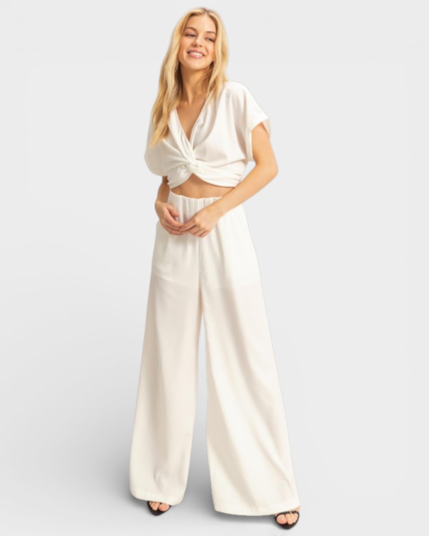 Woman wearing a white outfit with wide-leg pants on a light gray background