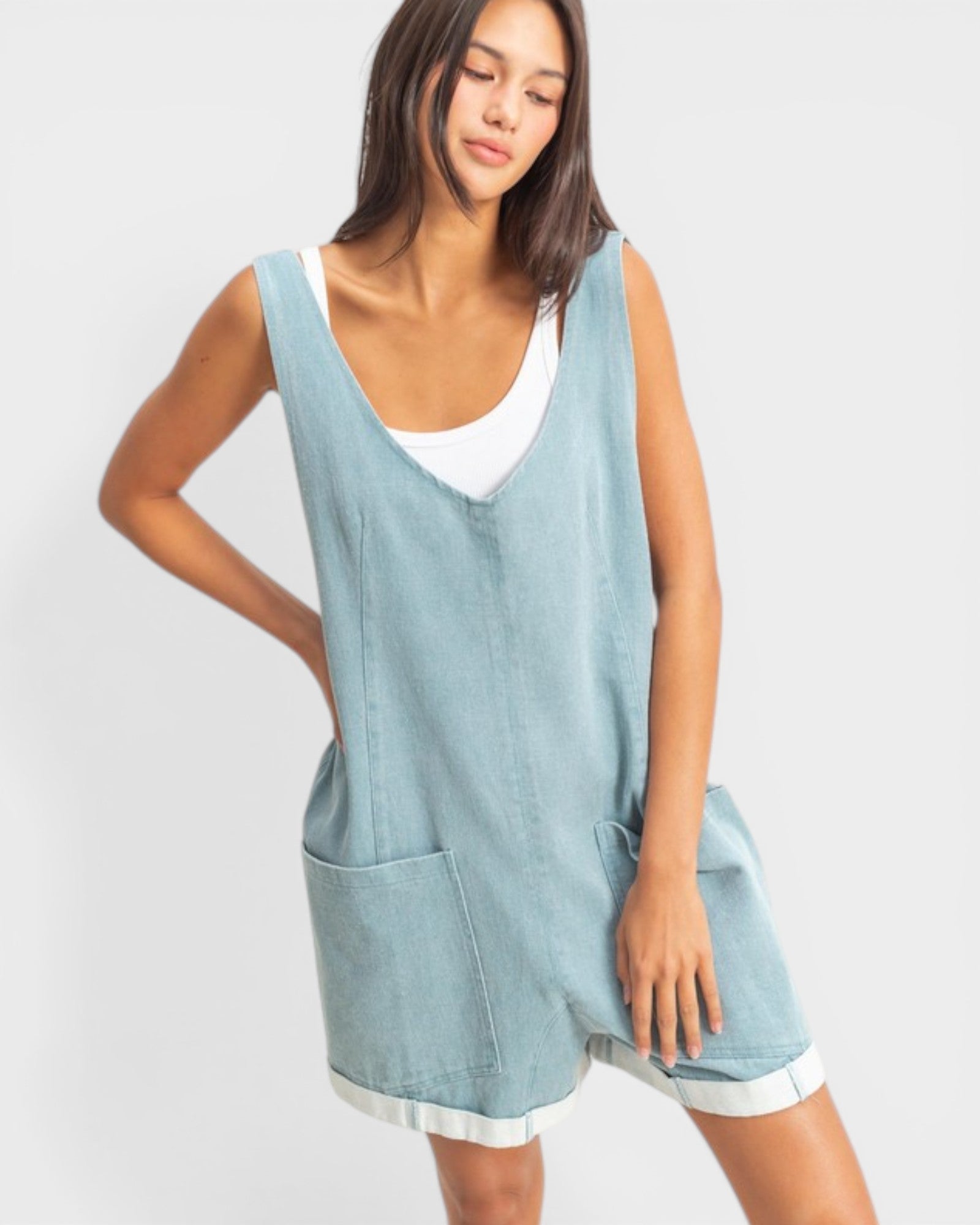 Woman wearing a light blue sleeveless dress with a white top underneath on a plain background