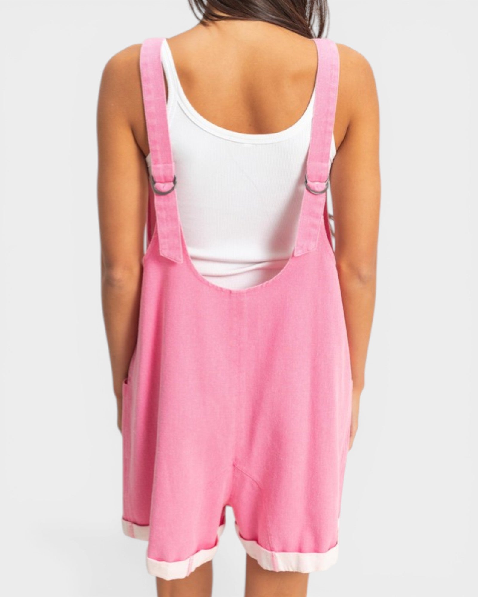 Person wearing a pink overall dress with a white top on a light gray background