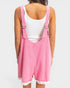 Person wearing a pink overall dress with a white top on a light gray background