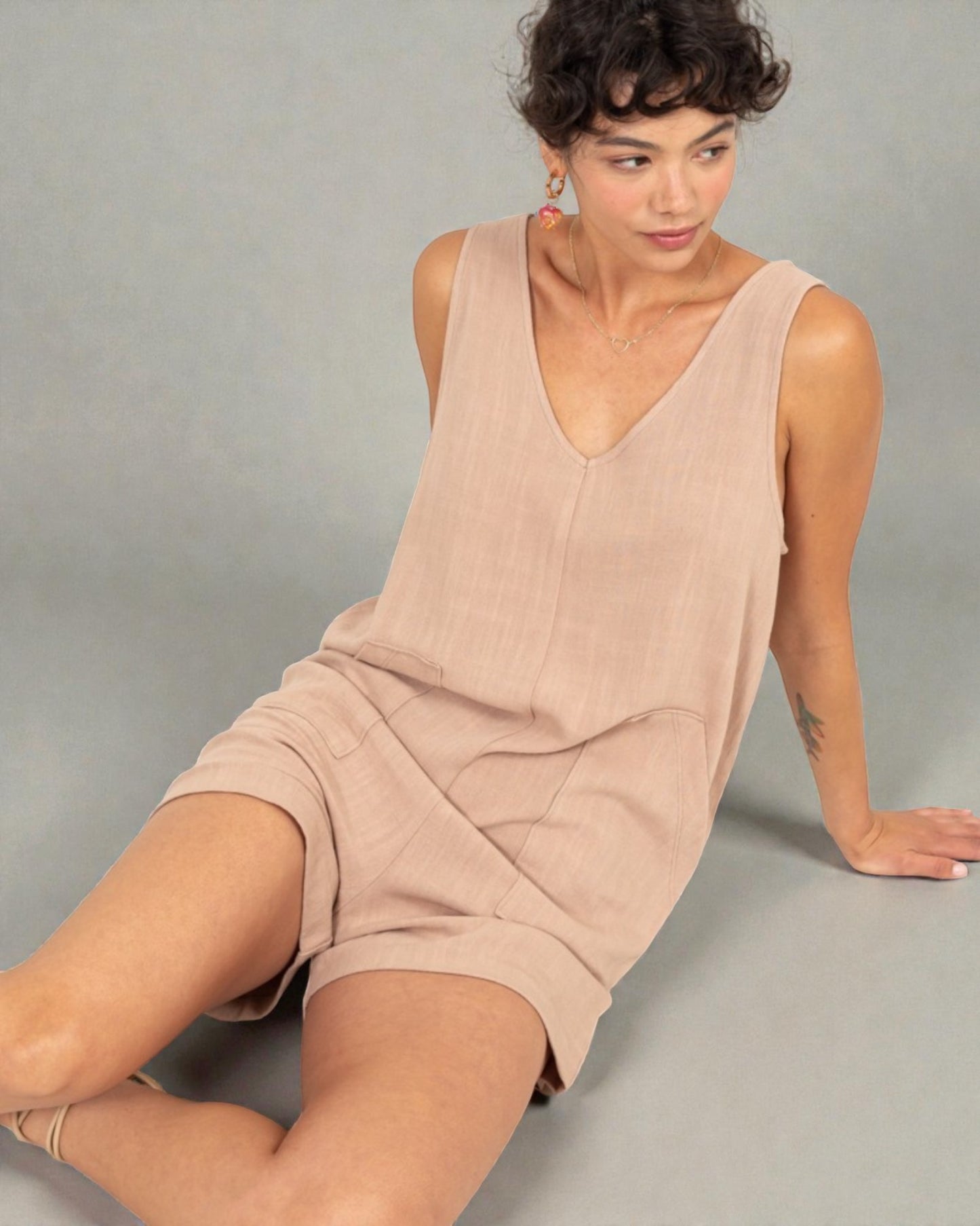Woman wearing a beige sleeveless dress sitting on a gray background