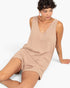 A woman wearing a sleeveless, v-neck beige linen romper, sitting against a plain white background.