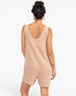 A woman shown from the back wearing a sleeveless, light beige romper with a deep V-neckline, set against a plain white background.