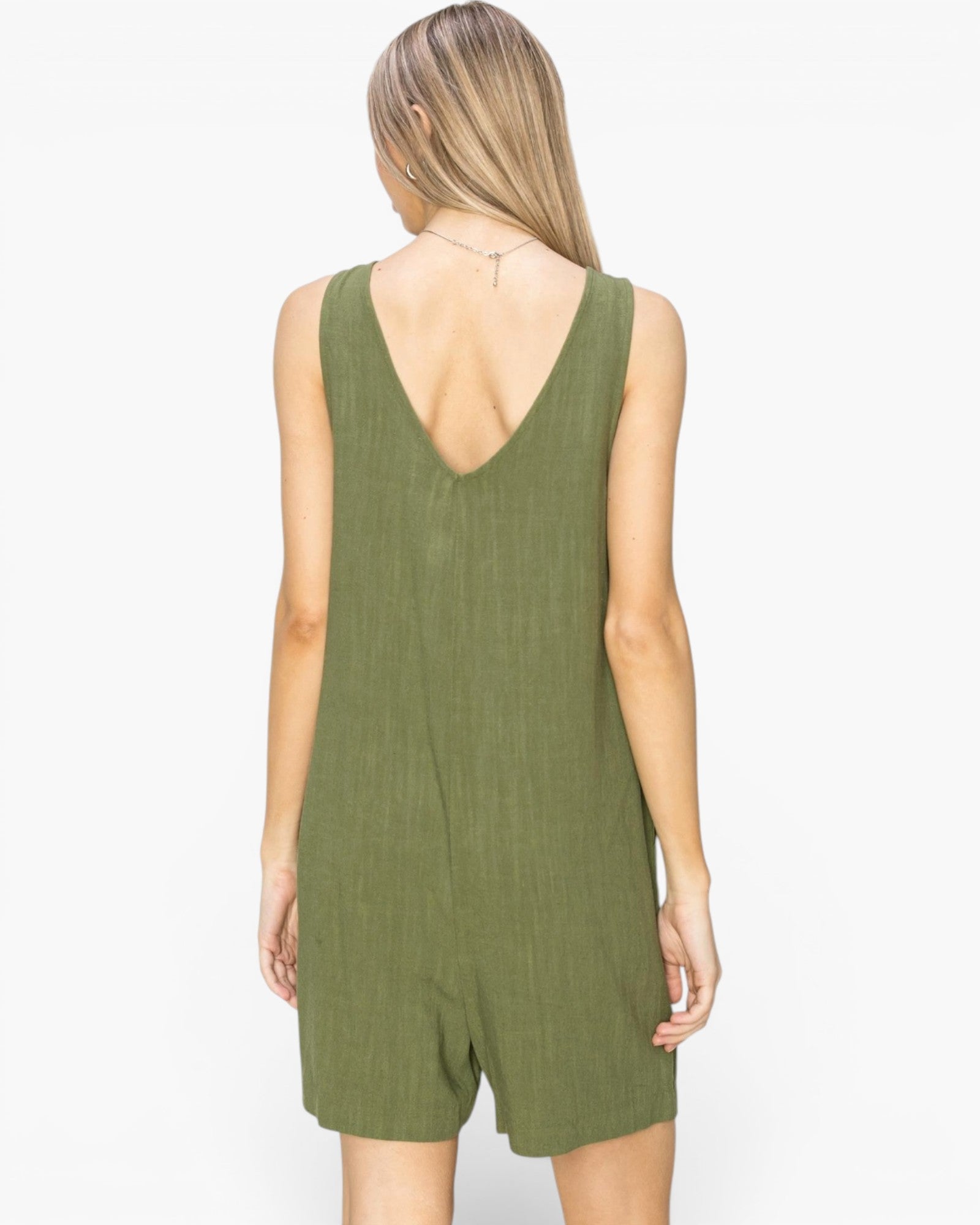 A woman viewed from the back wearing an olive green sleeveless romper with a deep V-neck and short legs, set against a plain white background.