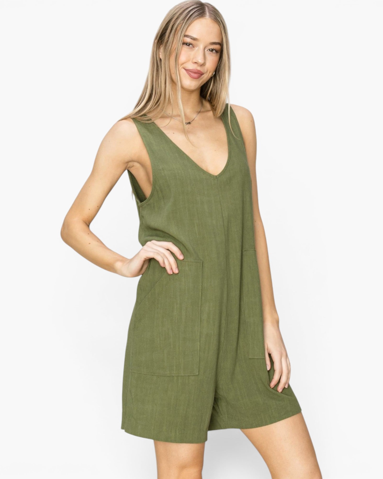 A woman modeling a sleeveless olive green romper with a V-neckline and front patch pockets, photographed against a clean white studio background.
