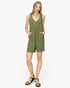 A woman modeling a sleeveless olive green romper with a V-neckline, front patch pockets, and short legs, paired with black strappy sandals against a plain white studio background.
