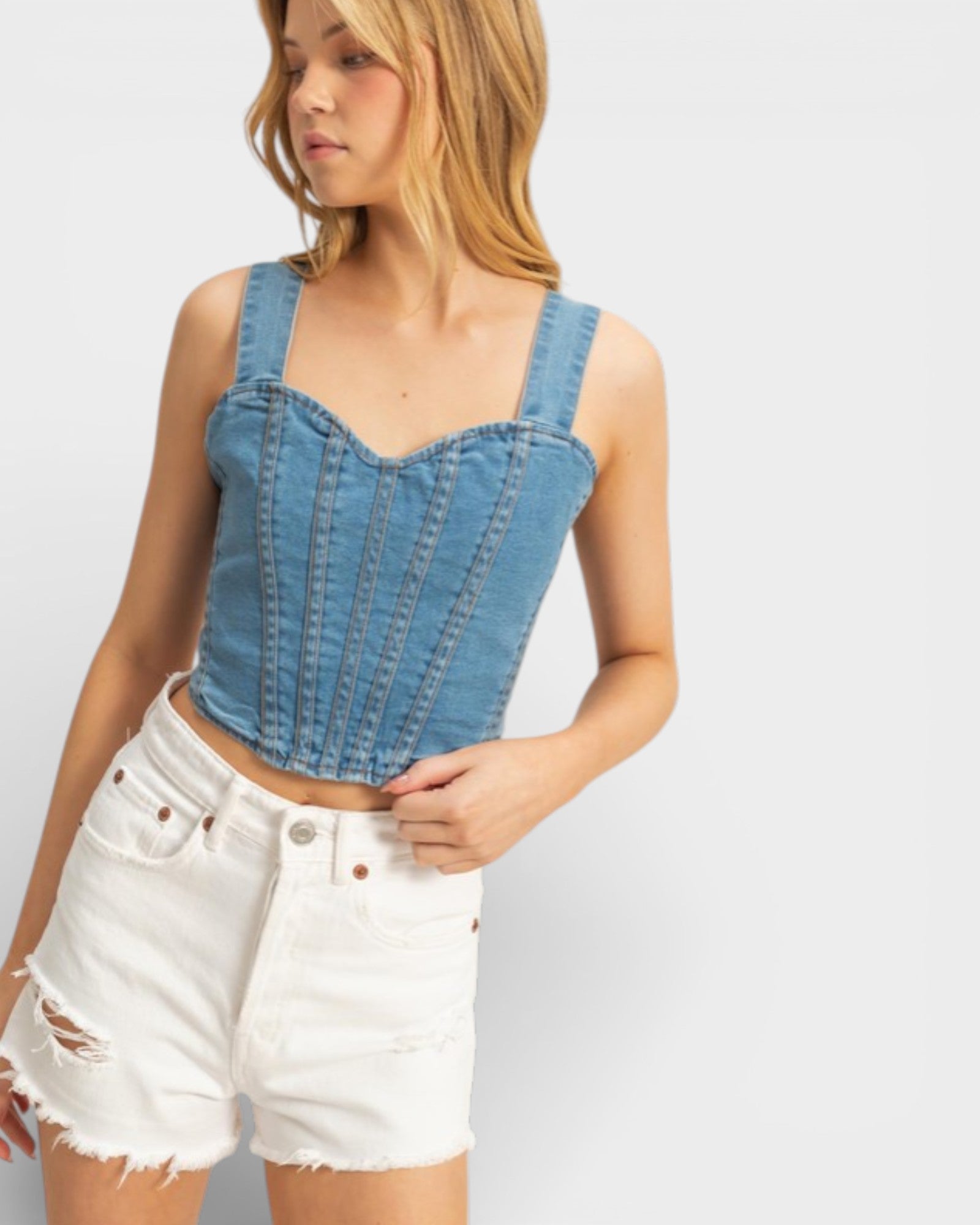 Woman wearing a denim corset top and white shorts on a plain background
