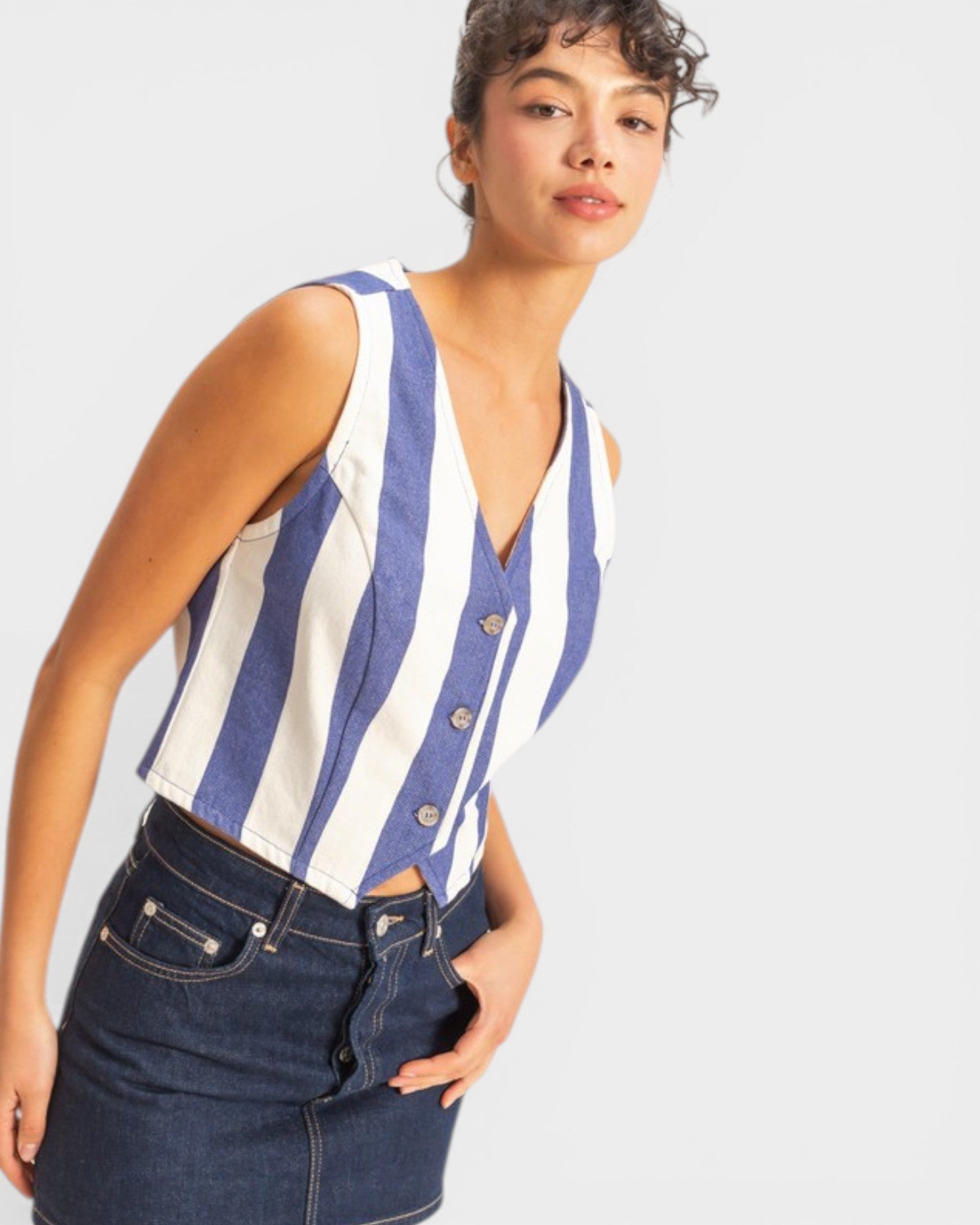 Woman wearing a blue and white striped sleeveless top with buttons, standing against a plain background.