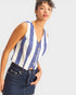 Woman wearing a blue and white striped sleeveless top with buttons, standing against a plain background.