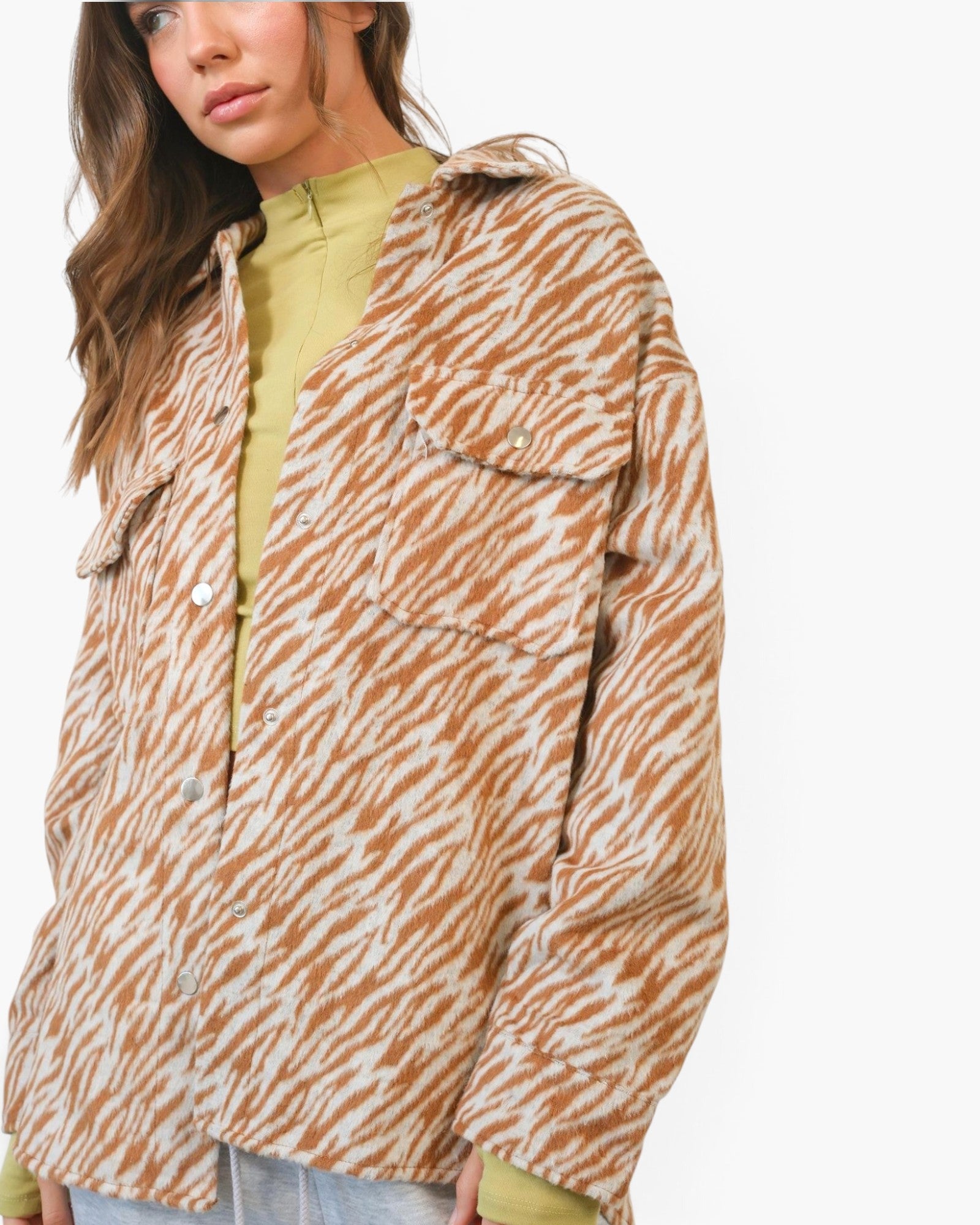 A woman wearing a brown and beige zebra-print overshirt over a light olive green mock-neck top, photographed against a clean white studio background.