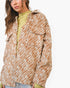 A woman wearing a brown and beige zebra-print overshirt over a light olive green mock-neck top, photographed against a clean white studio background.
