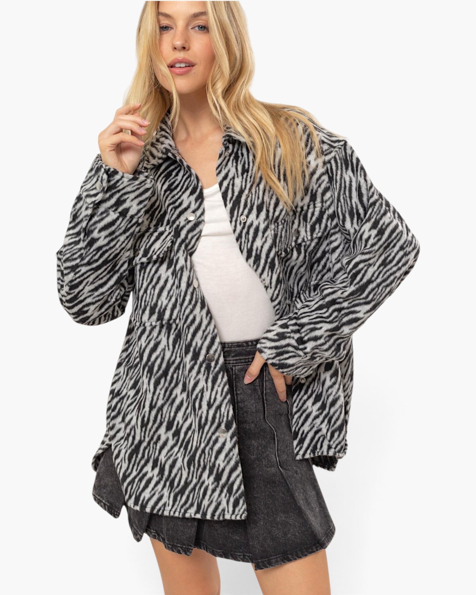 A woman modeling a black and white zebra-print button-up shirt jacket over a white tank top and a dark gray denim skirt, against a plain white studio background.