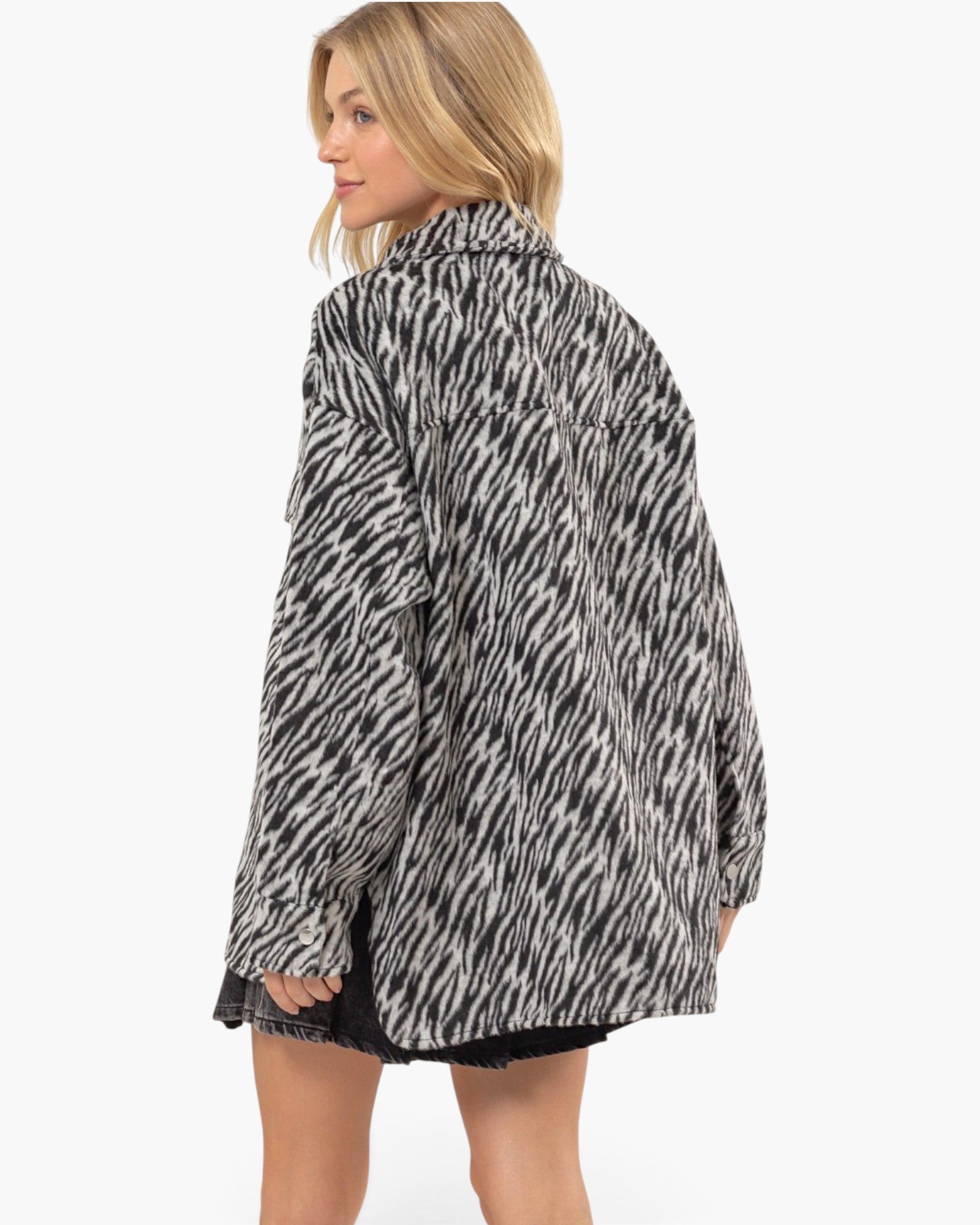 A woman shown from the back wearing an oversized black and white zebra-print shirt jacket, paired with a black denim skirt, against a plain white studio background.