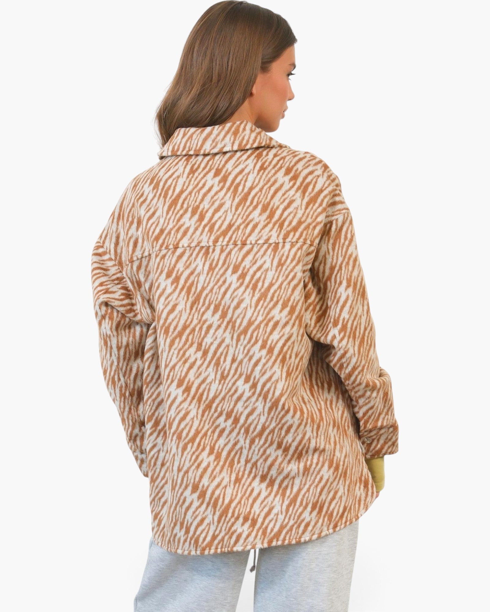 A woman shown from the back wearing a brown and white abstract patterned button-up shirt and light gray sweatpants, set against a plain white studio background.