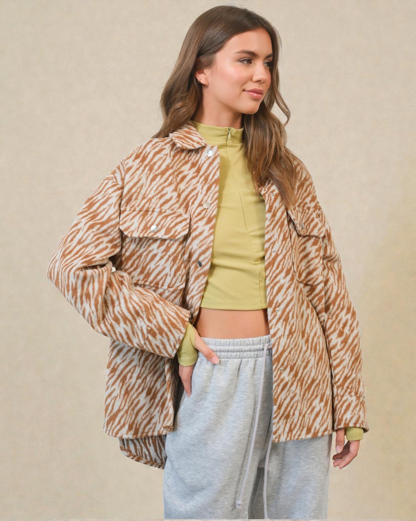 Woman wearing a patterned jacket over a green top and gray pants on a beige background