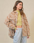 Woman wearing a patterned jacket over a green top and gray pants on a beige background