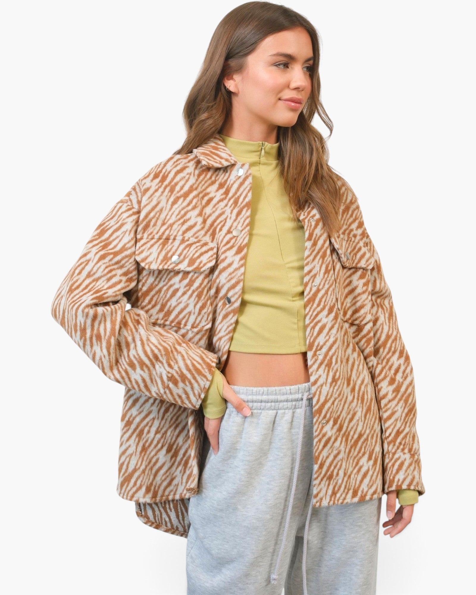 A woman modeling an oversized brown and beige zebra-print jacket over a yellow-green crop top and light gray sweatpants, photographed against a clean white studio background.