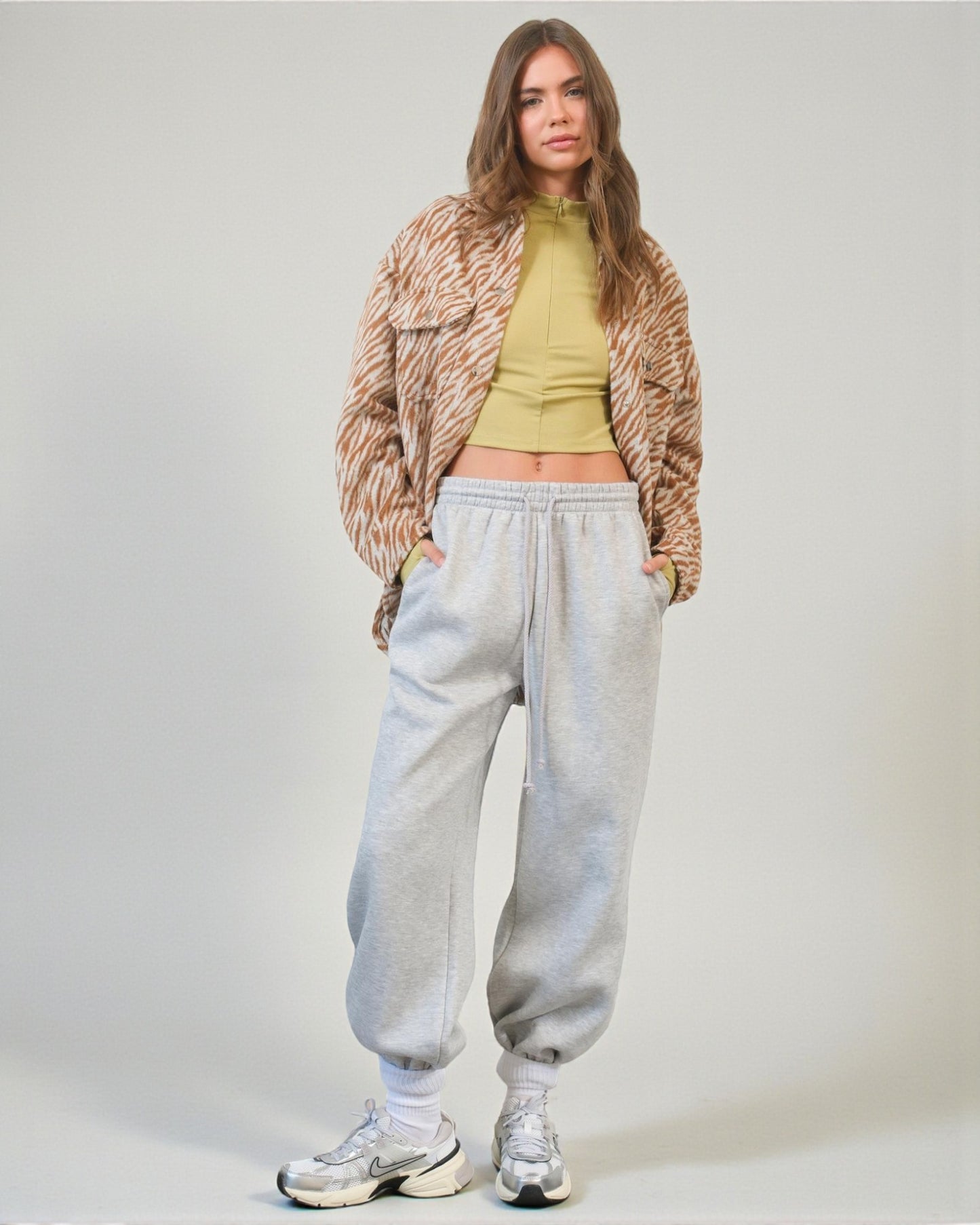 Person wearing a tiger print jacket, green top, gray sweatpants, and white sneakers on a plain background