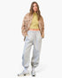 A model stands against a light gray studio background wearing a brown and beige animal-print cropped jacket over a yellow-green ribbed crop top, light gray sweatpants, white socks, and silver sneakers.