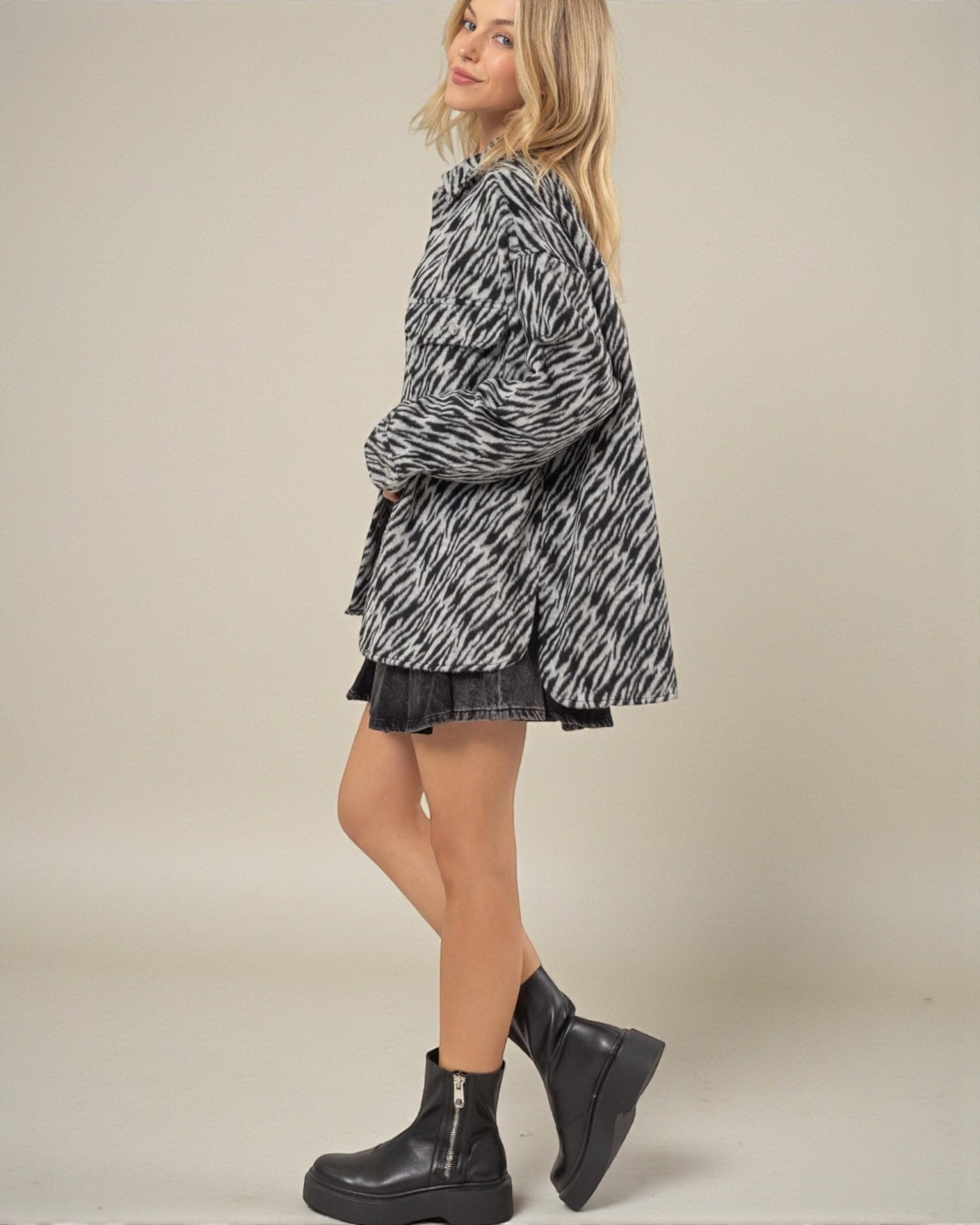 Woman wearing a black and white patterned jacket and black boots on a beige background