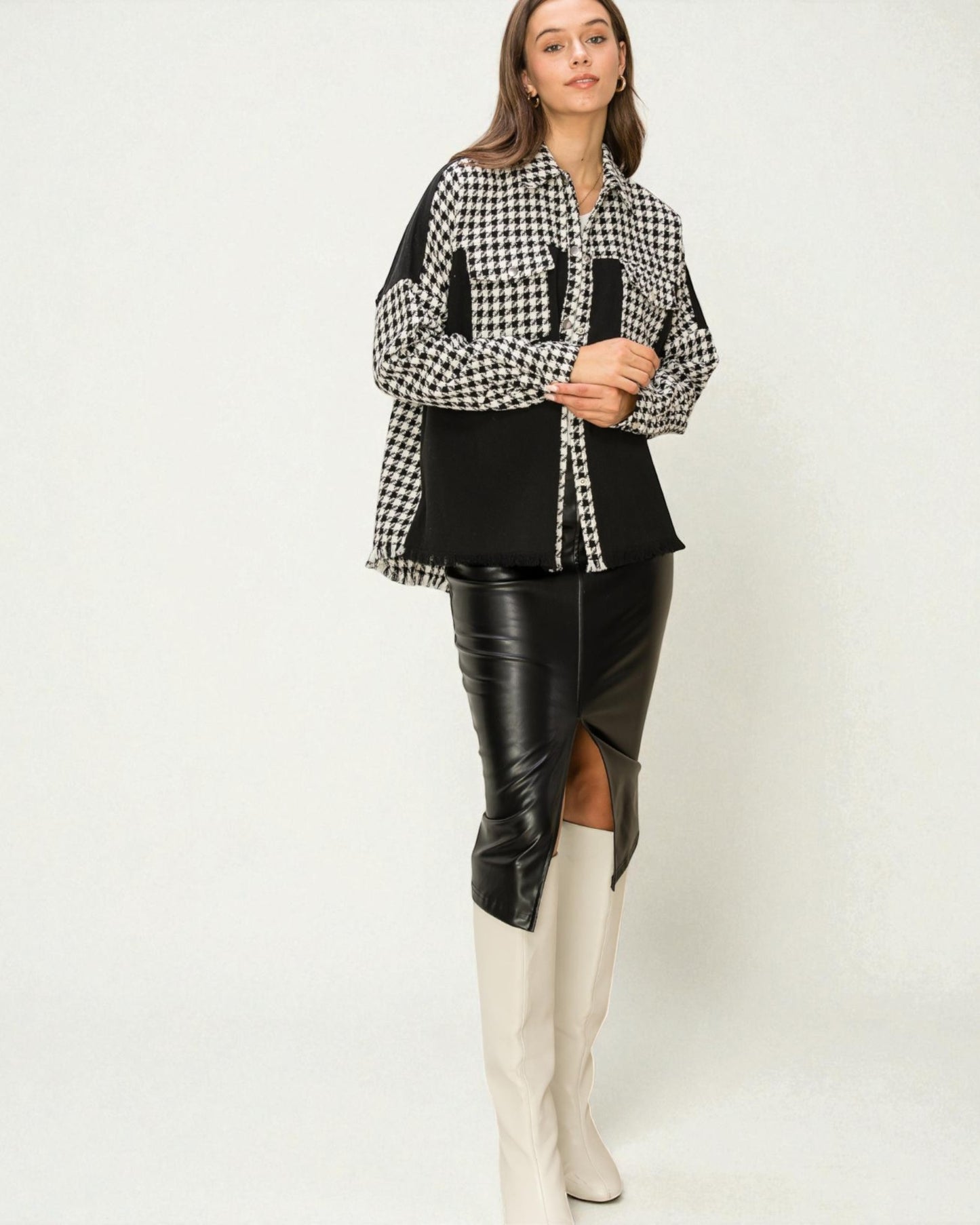 Woman wearing a black and white checkered shirt with a black leather skirt and white knee-high boots on a white background
