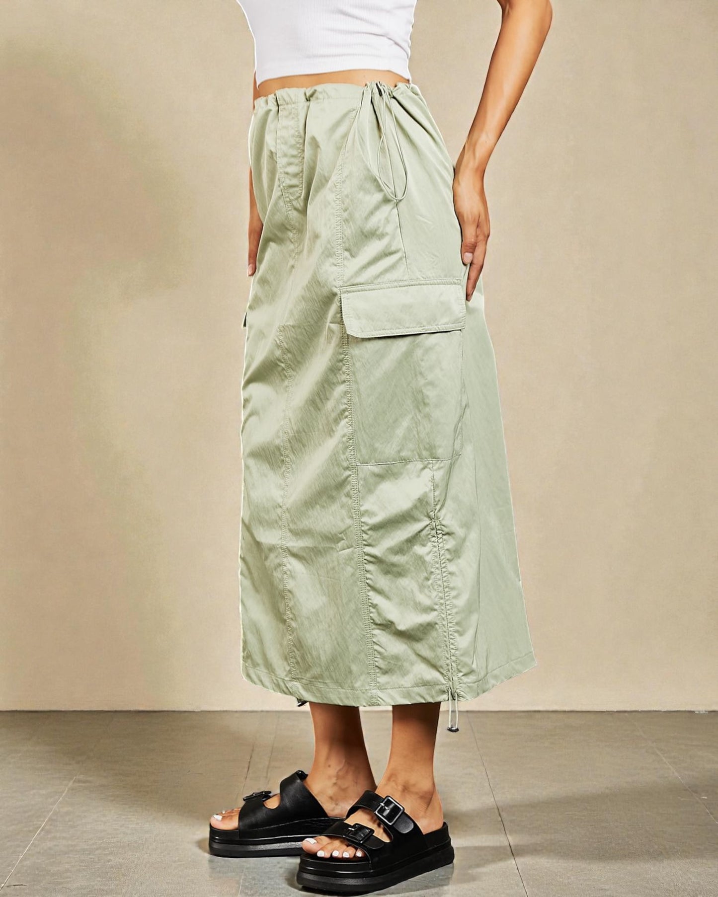 Person wearing a light green skirt with pockets on a beige background