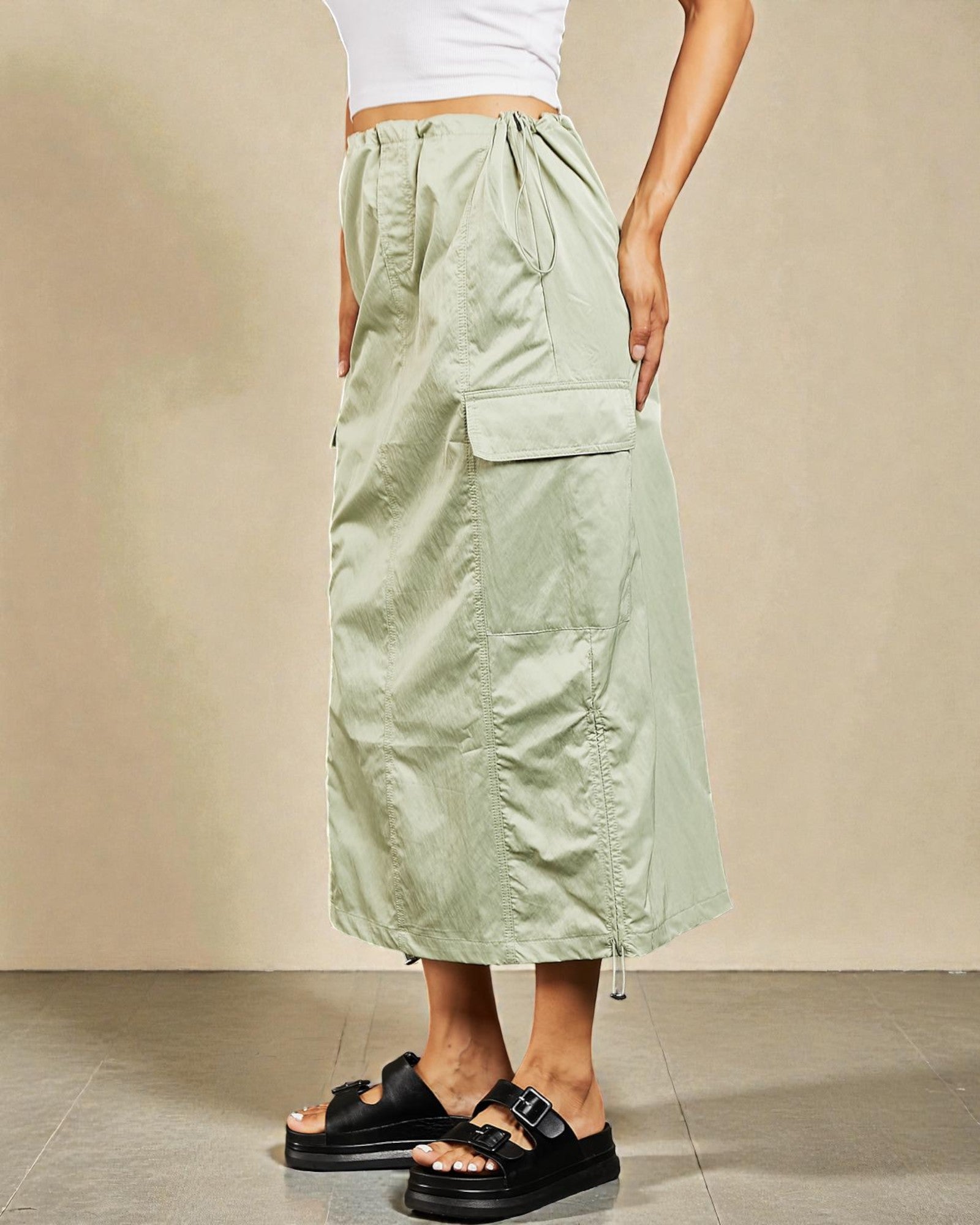 Person wearing a light green skirt with pockets on a beige background
