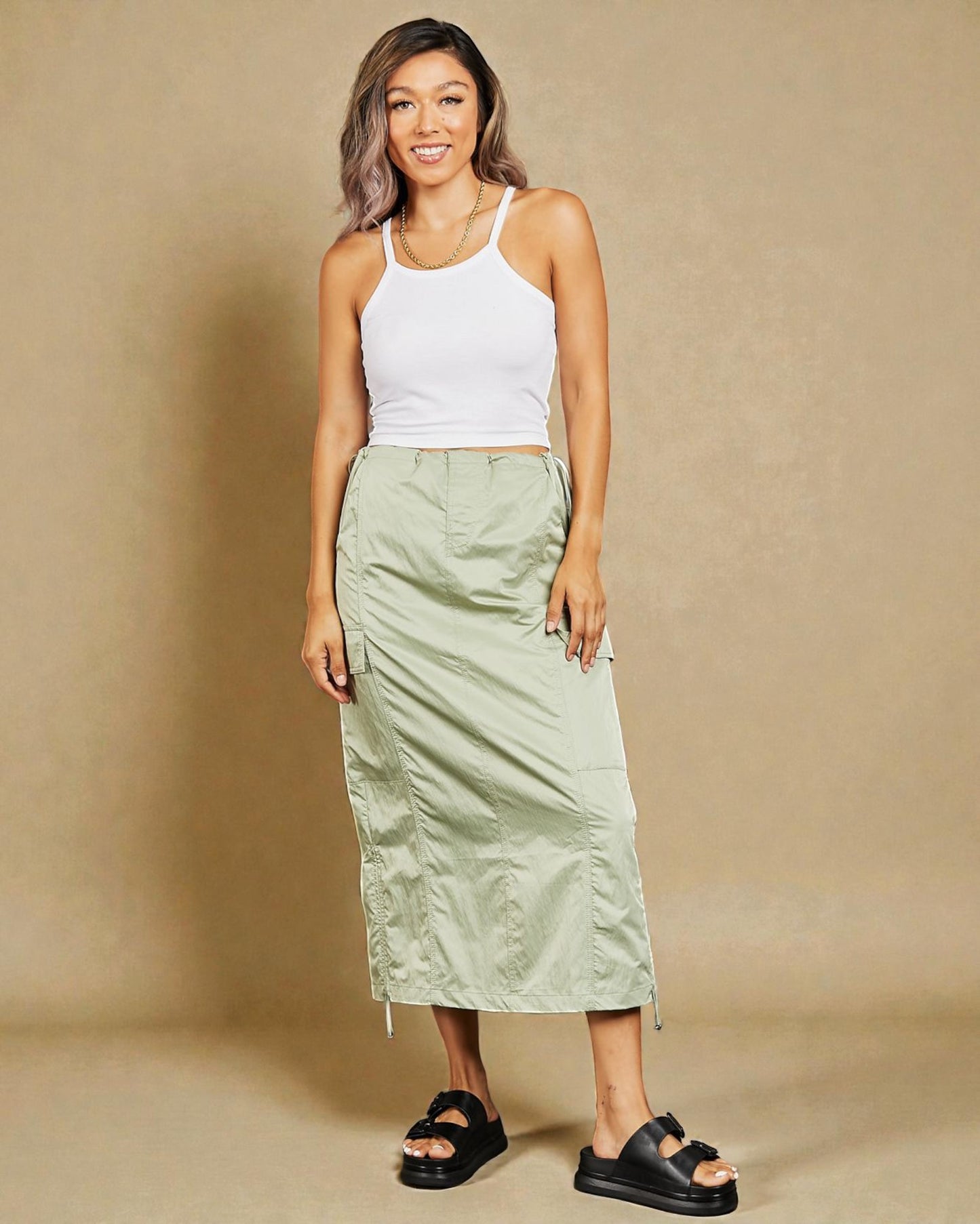 Woman wearing a white tank top and green skirt against a beige background