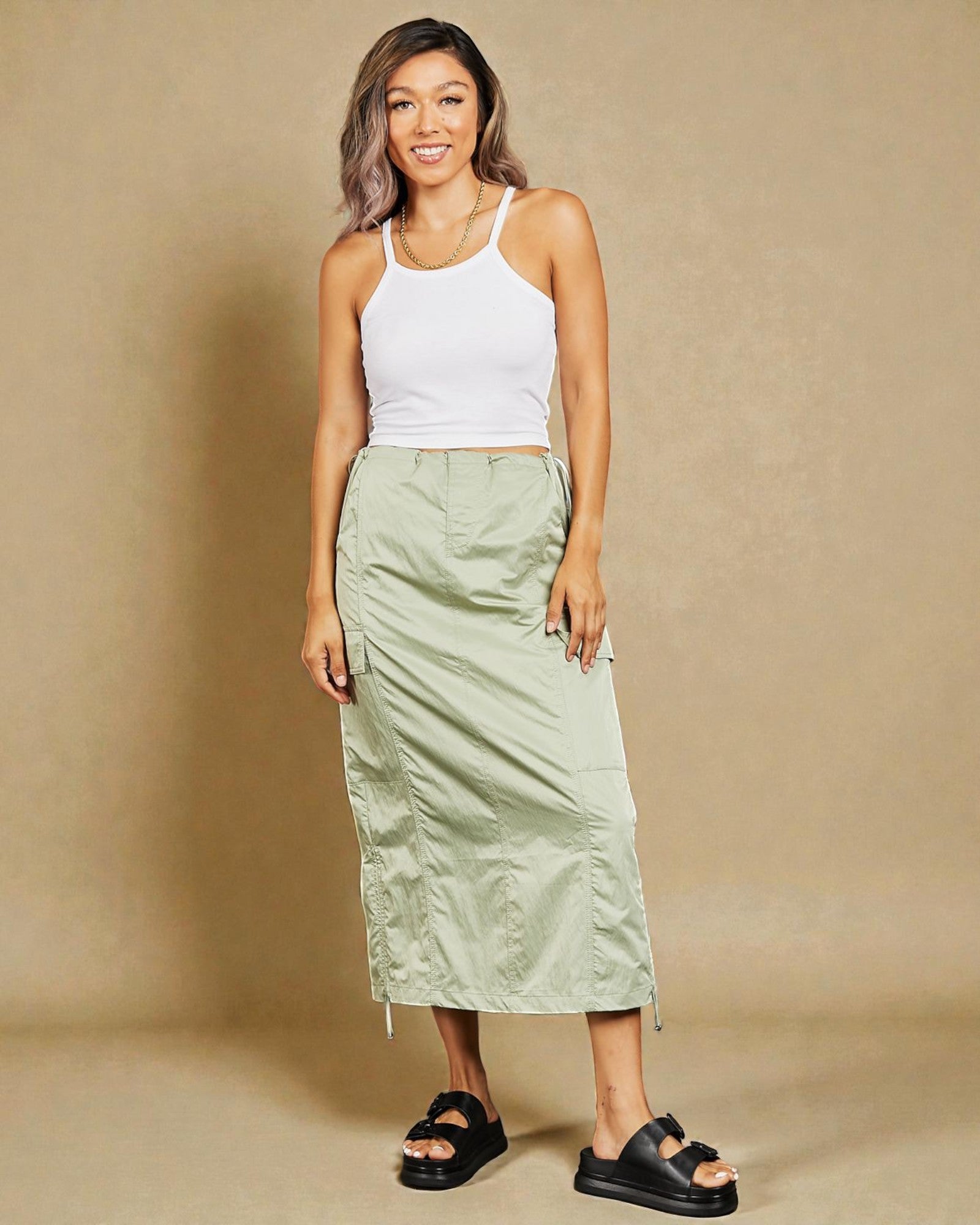Woman wearing a white tank top and green skirt against a beige background
