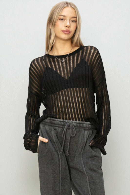 Woman wearing a black sheer long-sleeve top and gray sweatpants against a white background