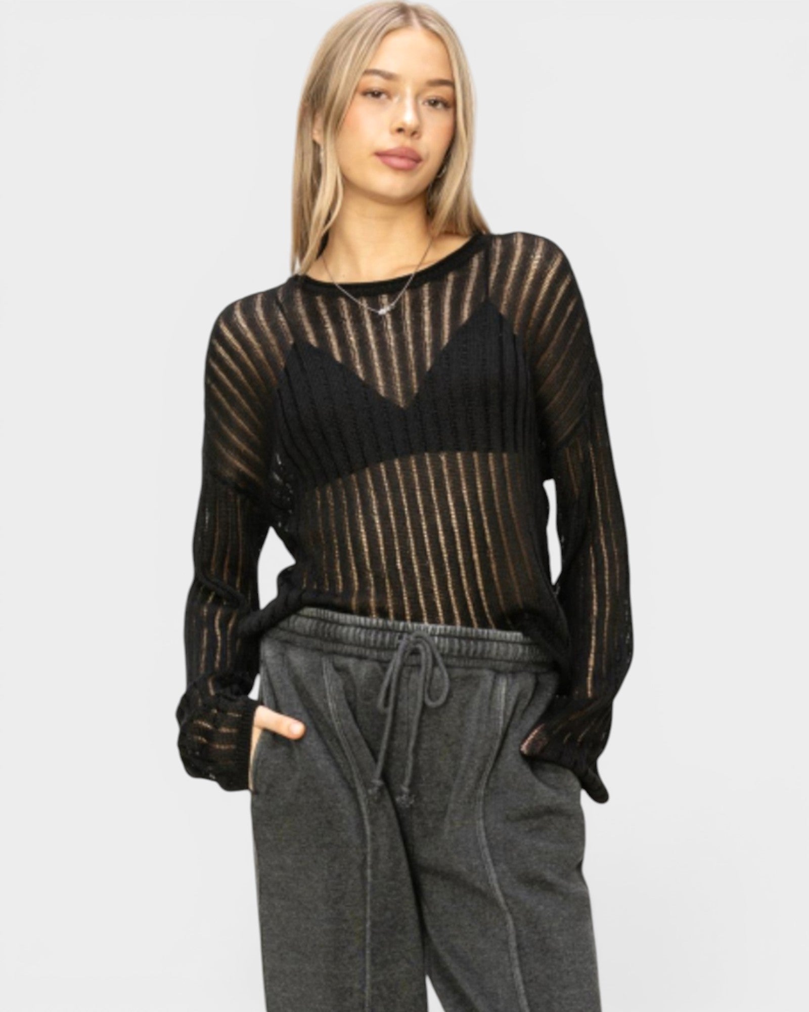Woman wearing a sheer black and gold sweater with gray pants on a white background
